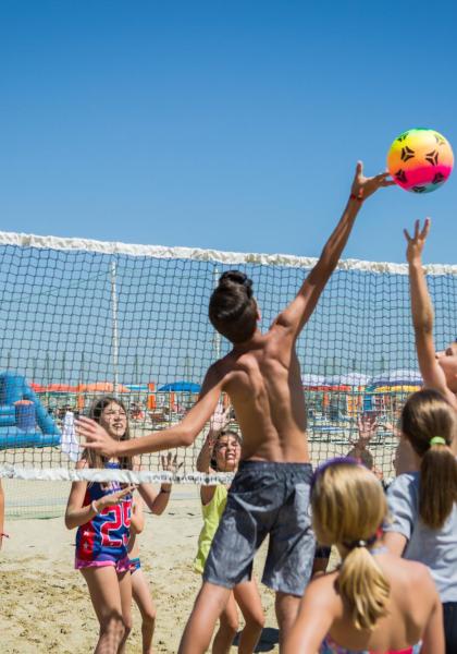Children play volleyball on the beach under the sun.