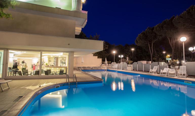 Beleuchteter Pool bei Nacht mit Liegestühlen und einem modernen Gebäude.
