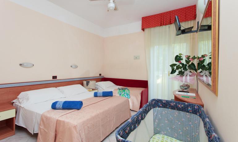 Camera d'albergo con letti, culla e pianta decorativa.