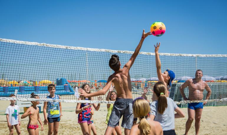 Giovani giocano a pallavolo sulla spiaggia sotto il sole estivo.