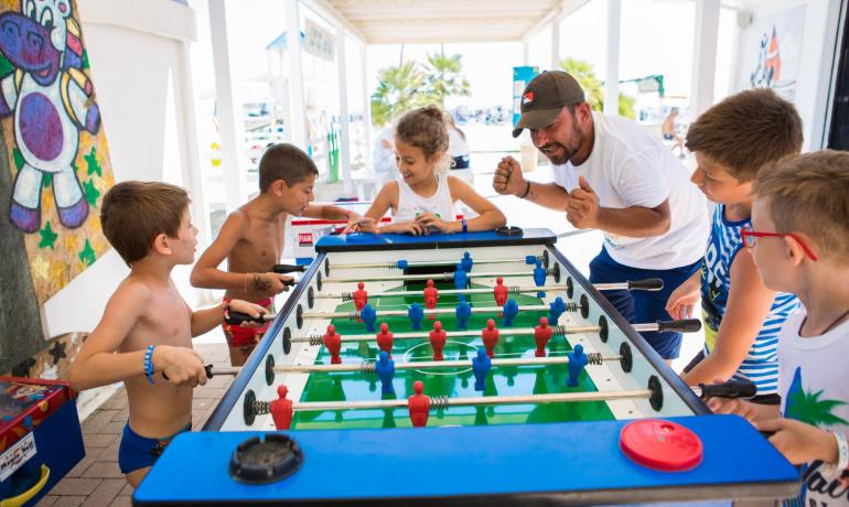 Children enthusiastically play foosball on a sunny day.