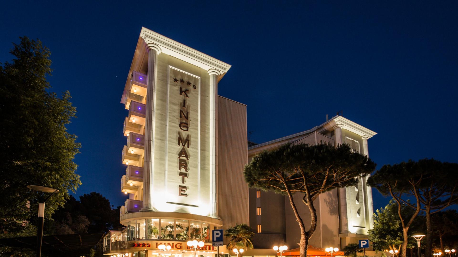 Hotel elegante illuminato di notte, atmosfera accogliente e rilassante tra alberi e luci.