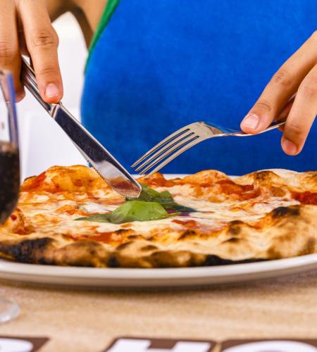 Mani tagliano pizza fumante, bicchiere di vino vicino.