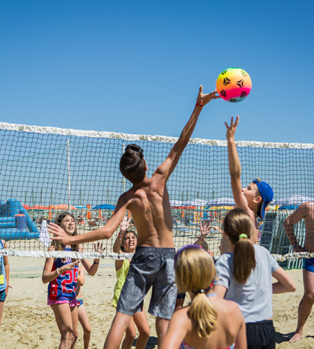 Ragazzi giocano a beach volley con entusiasmo sotto il sole estivo.