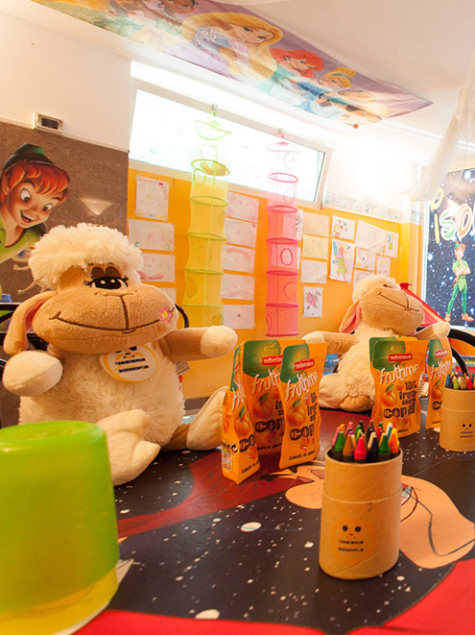 Area giochi per bambini con scivolo giallo e sedie colorate.