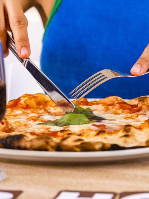 Mani tagliano pizza fumante, bicchiere di vino vicino.