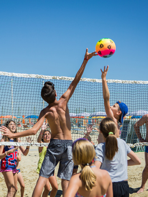 Ragazzi giocano a beach volley con entusiasmo sotto il sole estivo.